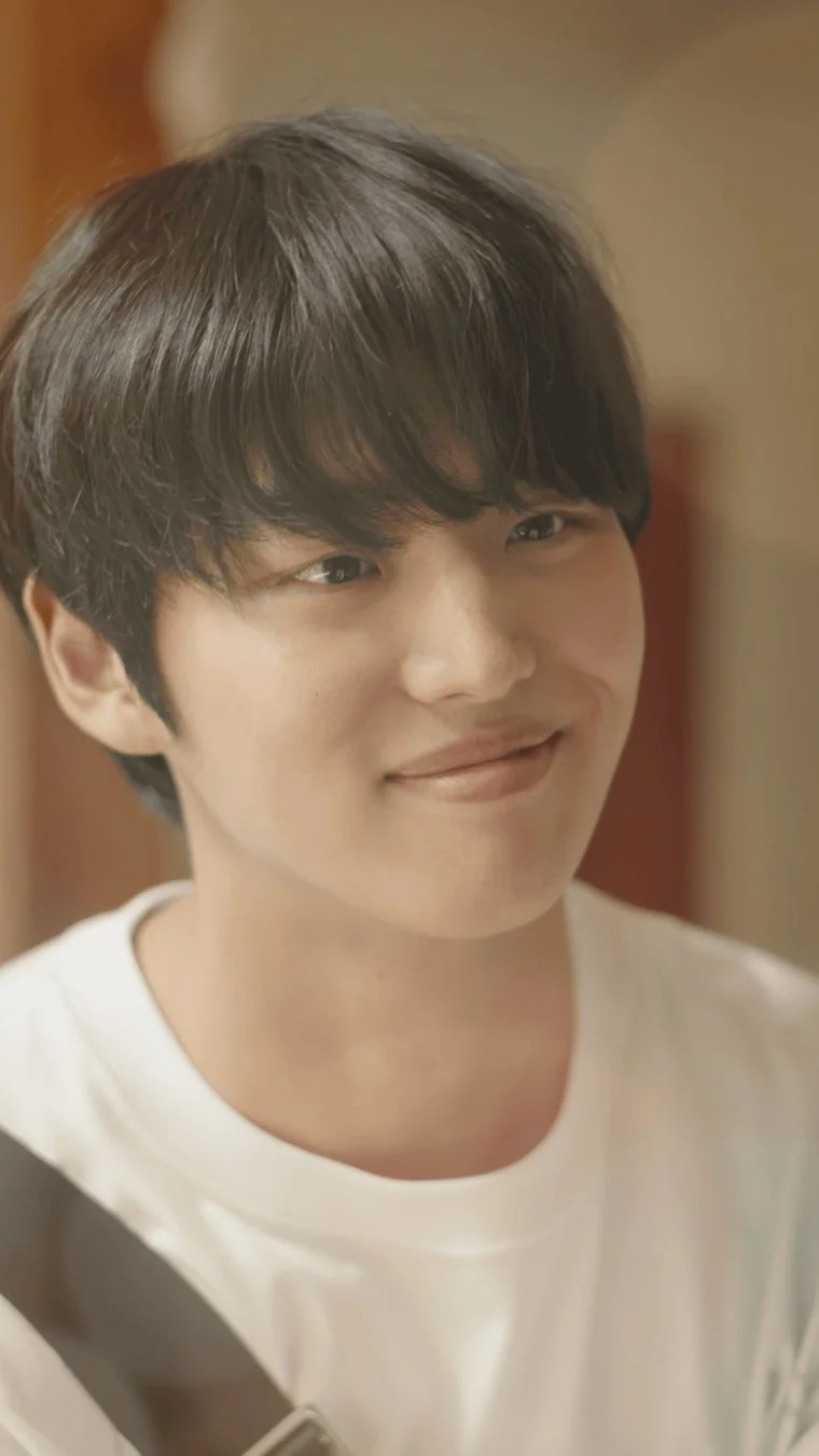 白いTシャツを着た若い男性の優しい笑顔のポートレート。黒髪で、暖色系のぼやけた背景を背にしています。