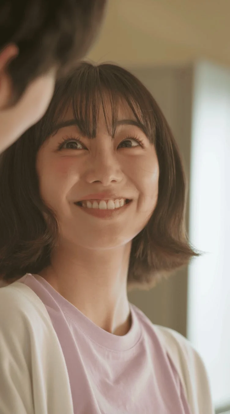 明るい笑顔を見せる若い女性のポートレート。短めの髪と前髪が特徴で、誰かを見上げている。幸せそうな表情が印象的で、暖かく親密な雰囲気が伝わる。