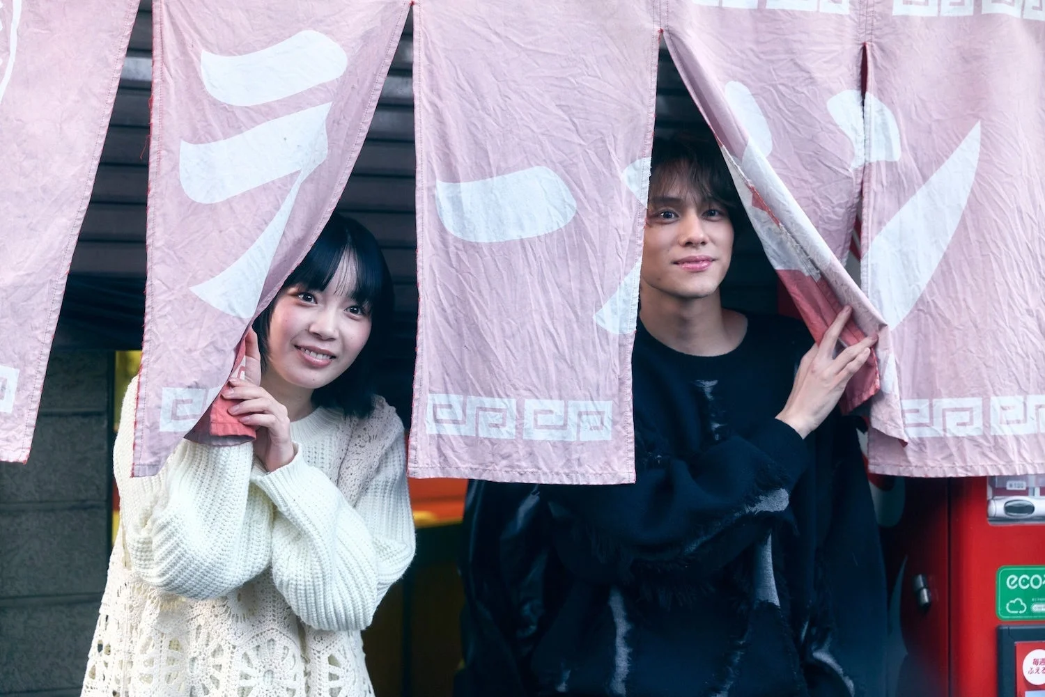 ラーメン屋の暖簾から顔を出す男女