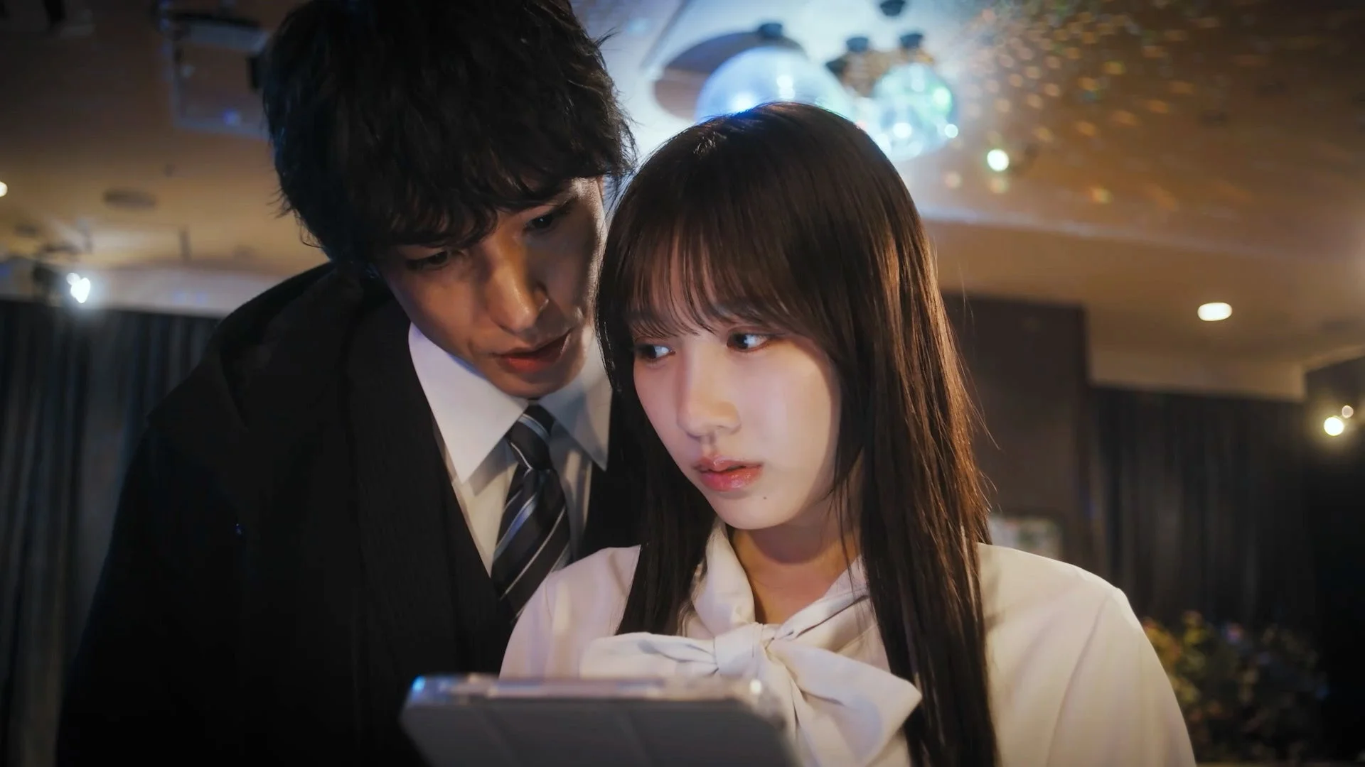 スーツ姿の男性が女性の肩越しにタブレットを覗き込む