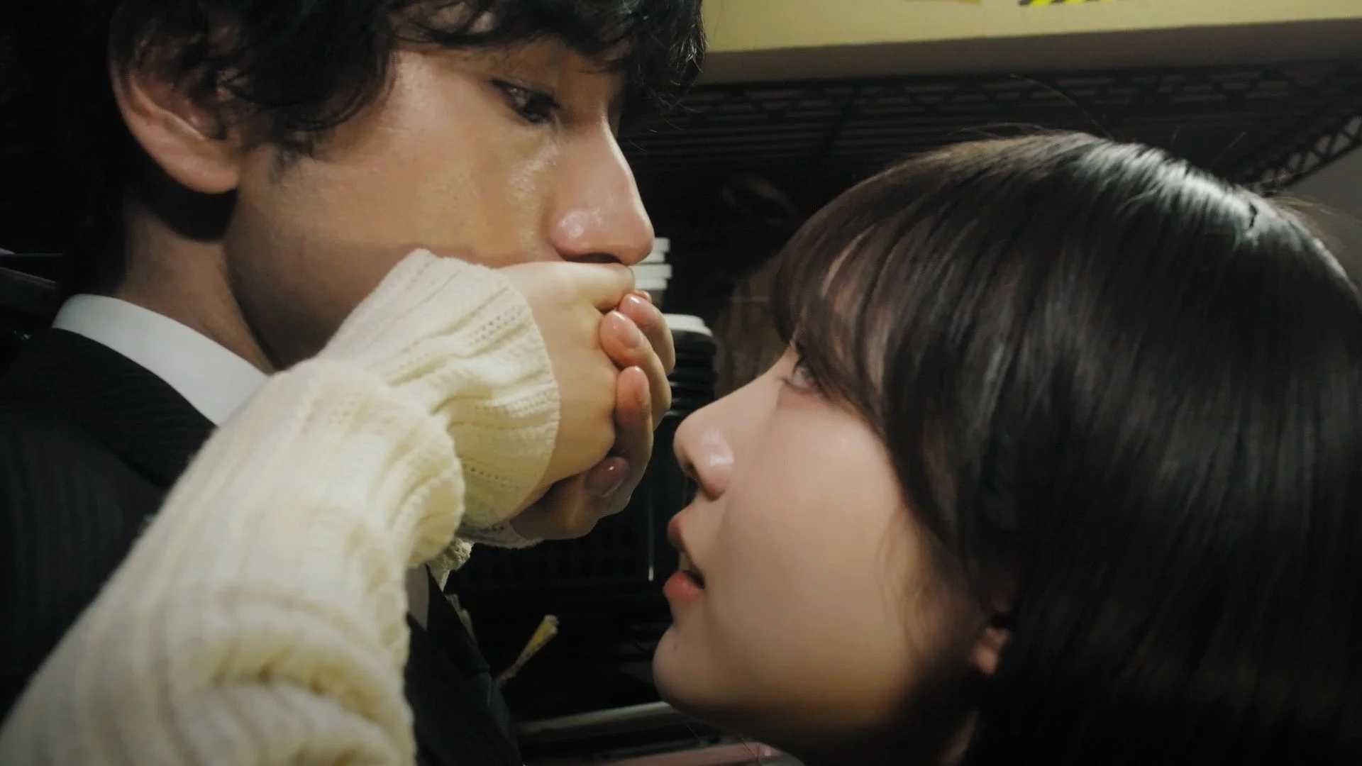 男女が顔を近づけ、女性が男性の口を手で塞ぐ