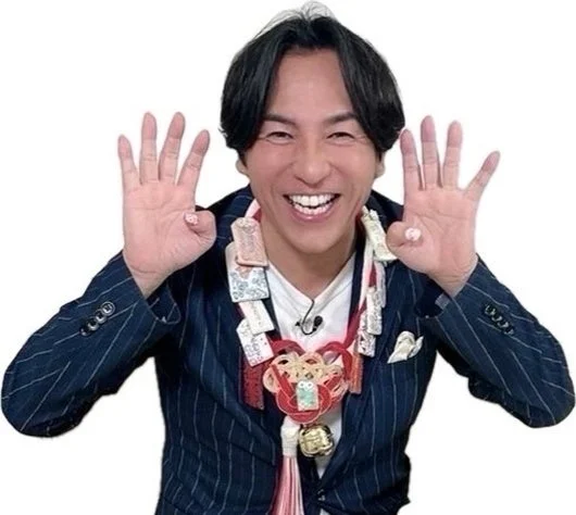 ストライプのスーツを着た男性が、首にたくさんのお守りや縁起物を飾り、満面の笑みで両手を広げている