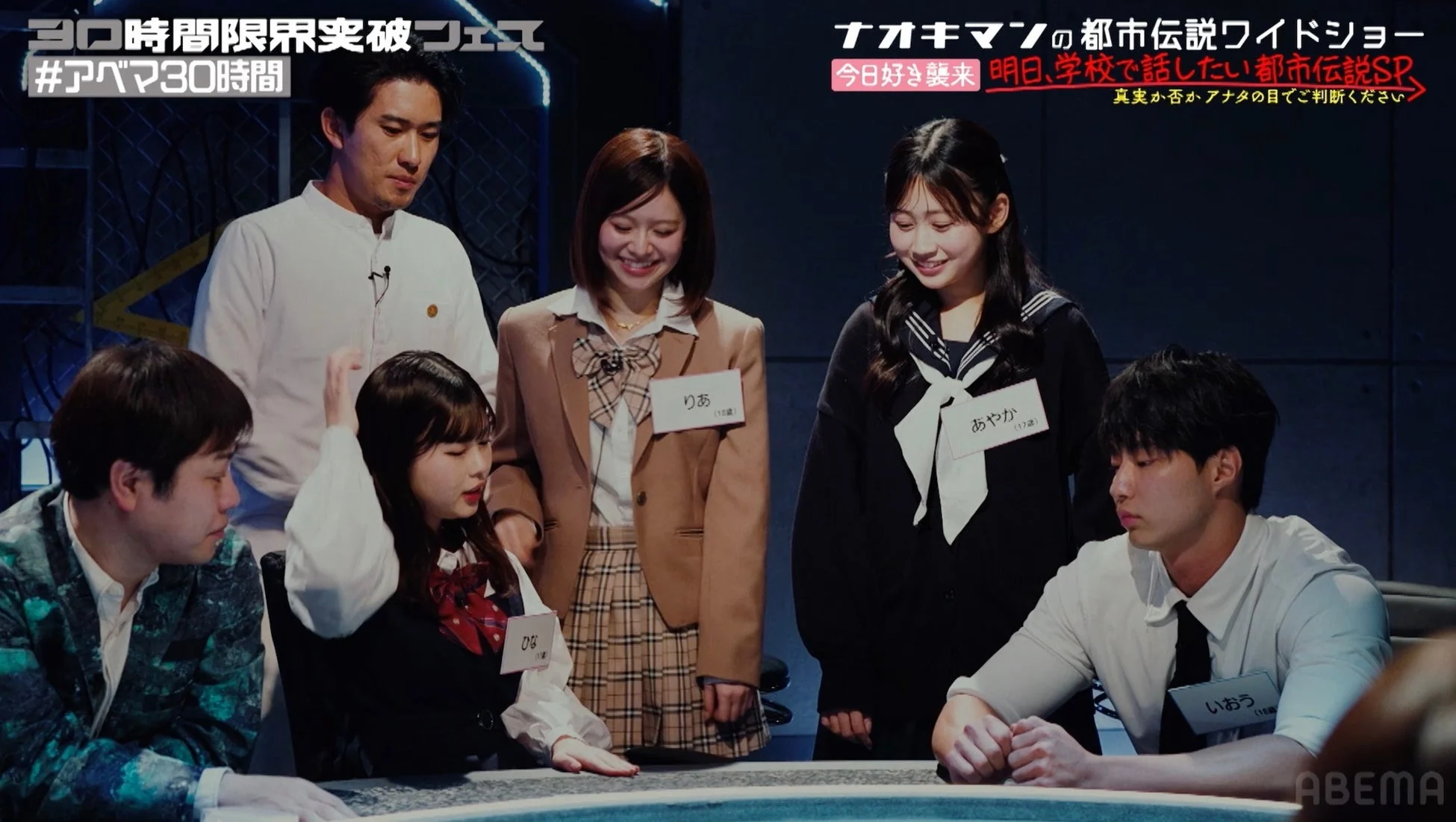 「ナオキマンの都市伝説ワイドショー」の一場面で、複数の若者がスタジオに集まっている。番組は「明日、学校で話したい都市伝説SP」と題され、出演者たちは学生服姿で都市伝説について語り合うトークバラエティ番組の収録風景と見られる。