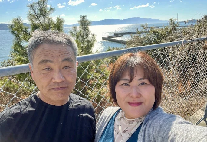 晴れた日に海辺で自撮りをする日本人カップルの写真